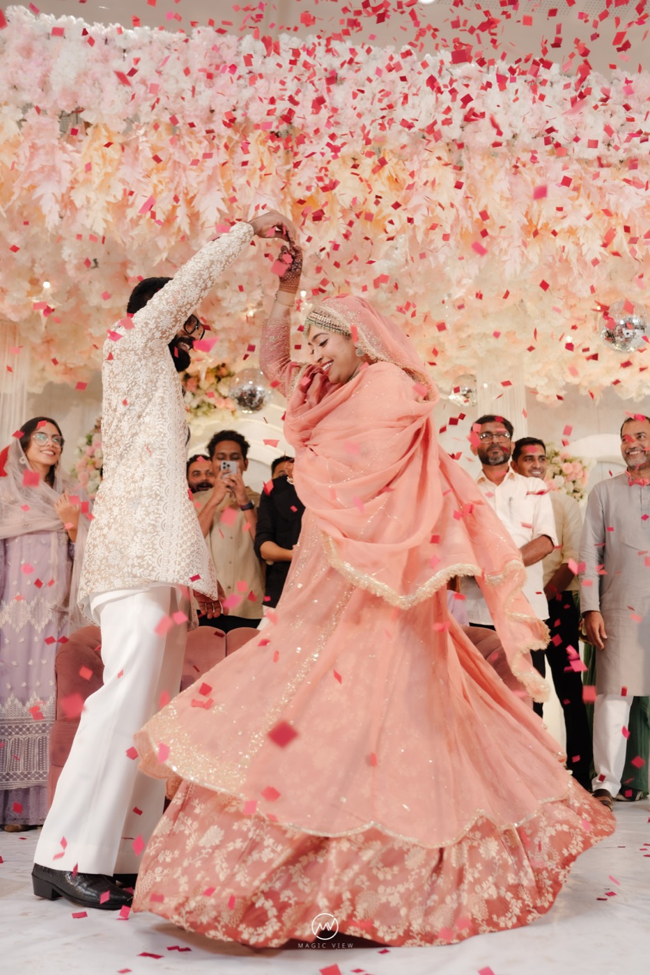 The couple celebrating beneath rose-coloured confetti